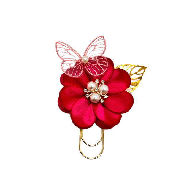 Decorative paper clip or bookmark with red flower, butterfly, and pearl embellishments on a white background